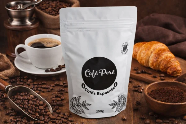 Café Perè: Grãos de café especiais, embalagem de 250g, com xícara, croissant e moedor ao fundo.